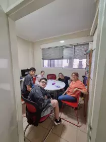 En la imagen se ve a un grupo de adolescentes sentados al rededor de una mesa redonda junto a la directora de la institución.